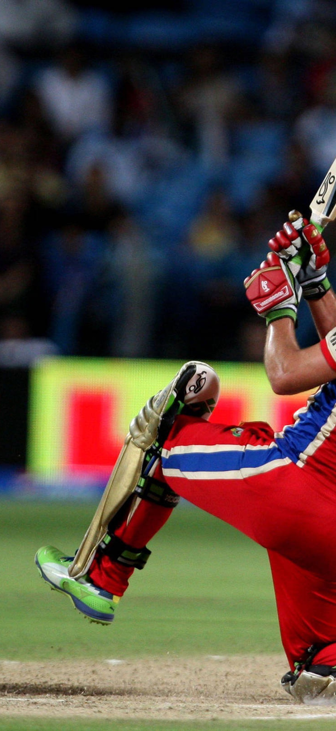 Cricket player hitting a ball during a night match with crowd in background.