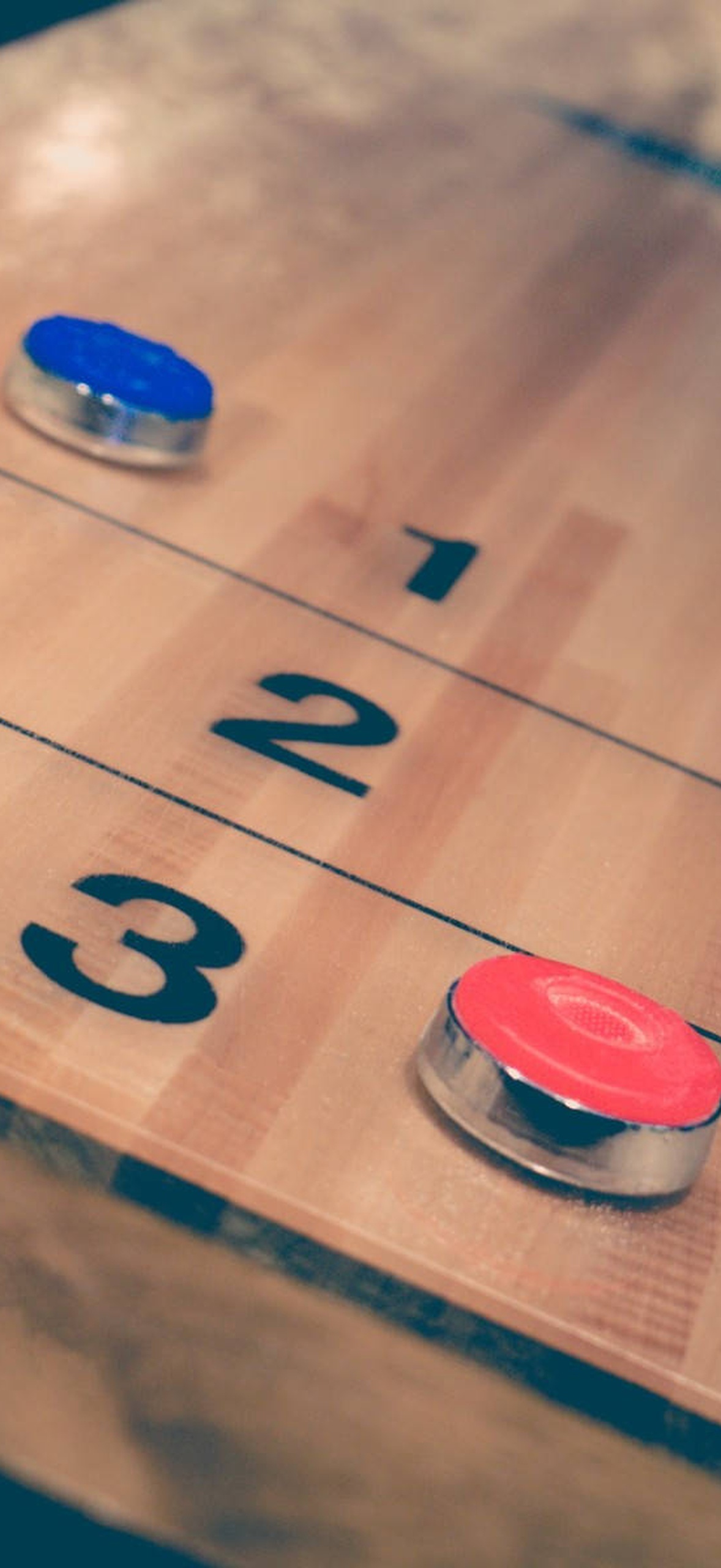Red and blue shuffleboard pucks on a wooden scoring board with numbered lines.