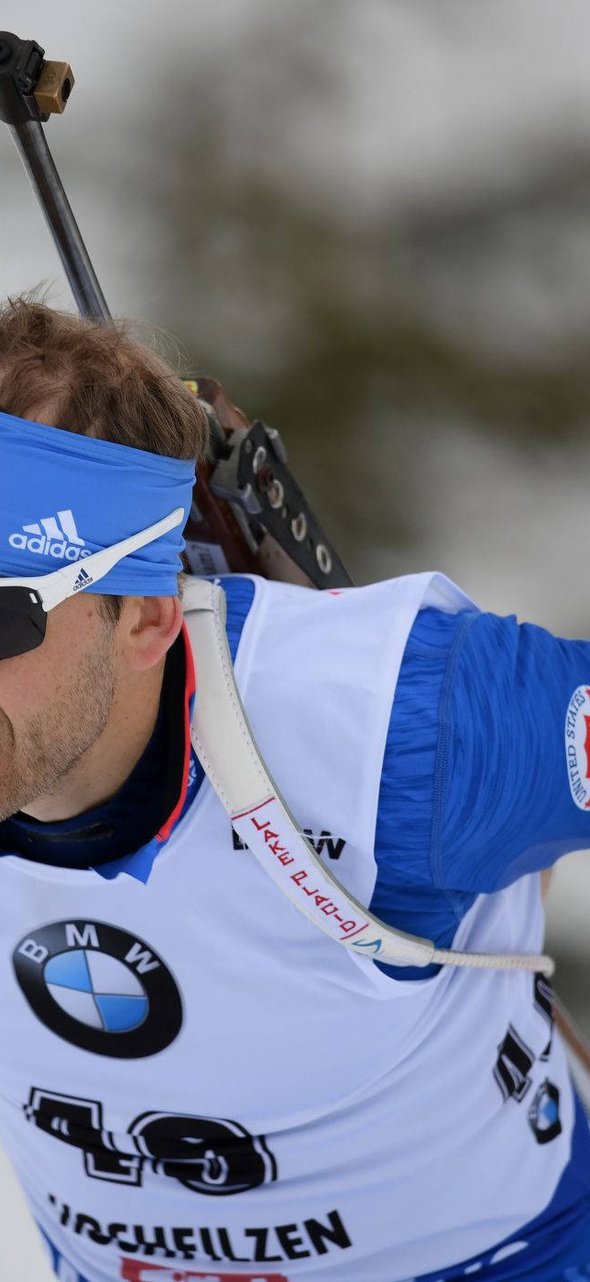 Biathlete aiming rifle while skiing in snowy winter landscape.