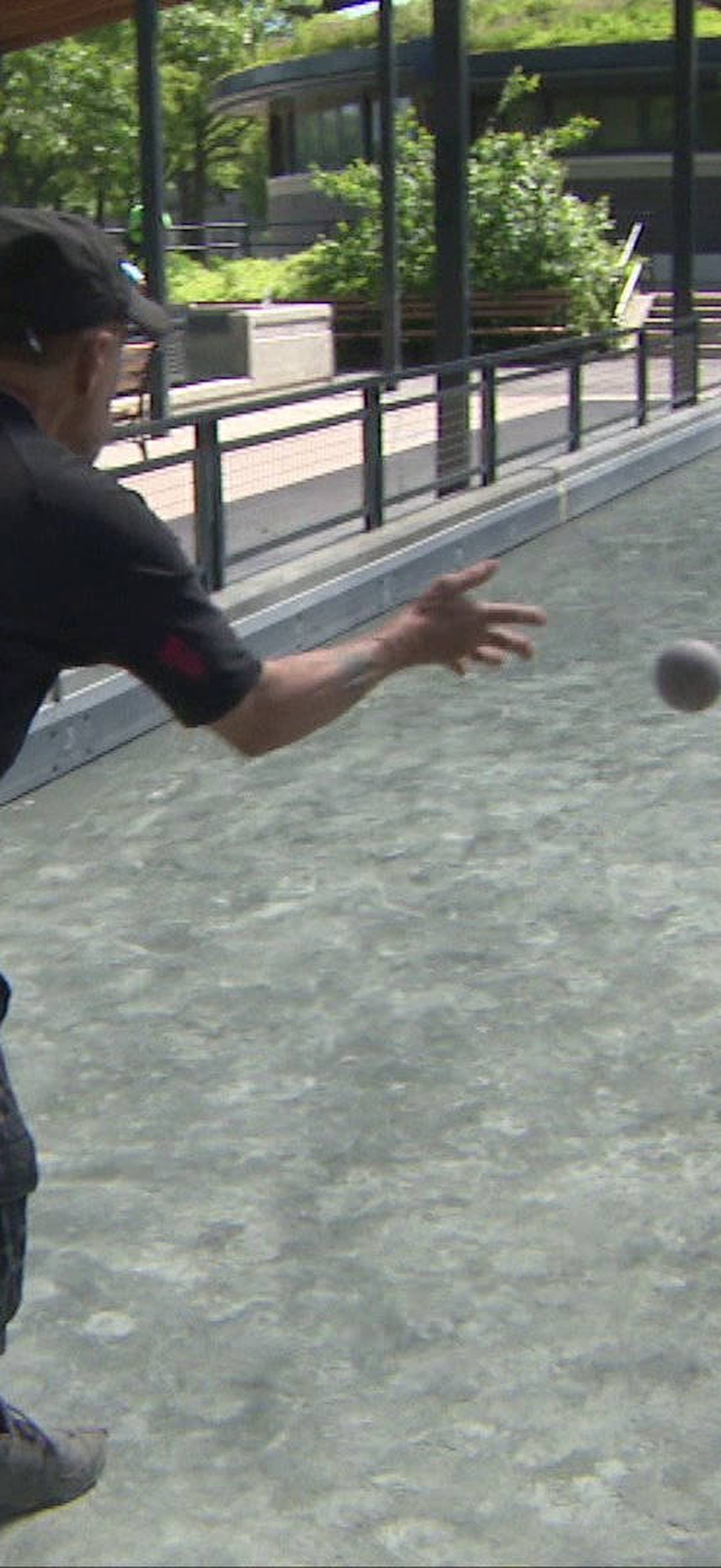 Man playing bocce ball in a sunny outdoor court with spectators.