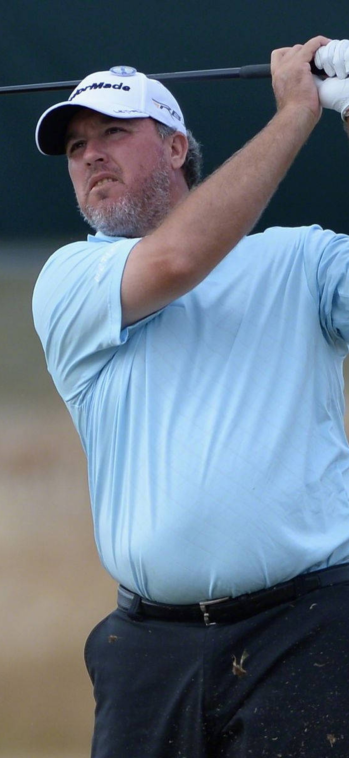 Golfer swinging club with intense focus during outdoor game.