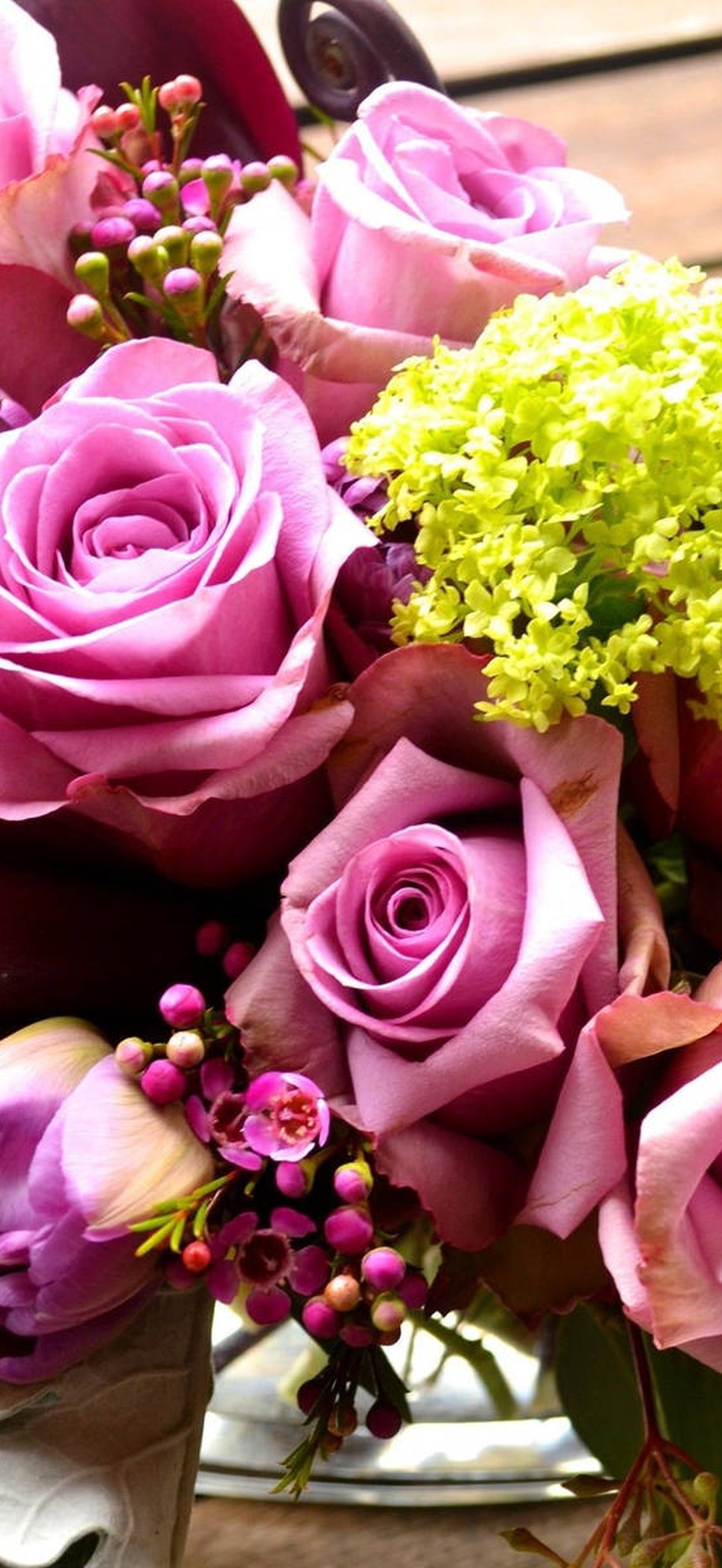Vibrant floral arrangement with pink roses calla lilies and green hydrangeas in glass vase on wood.