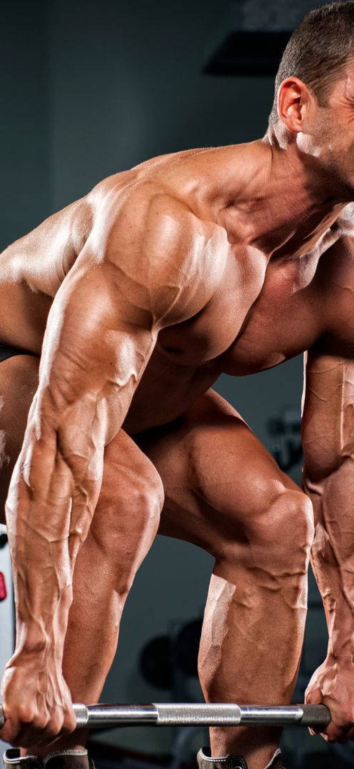 Athlete lifting heavy barbell in gym with defined muscles and focused expression.