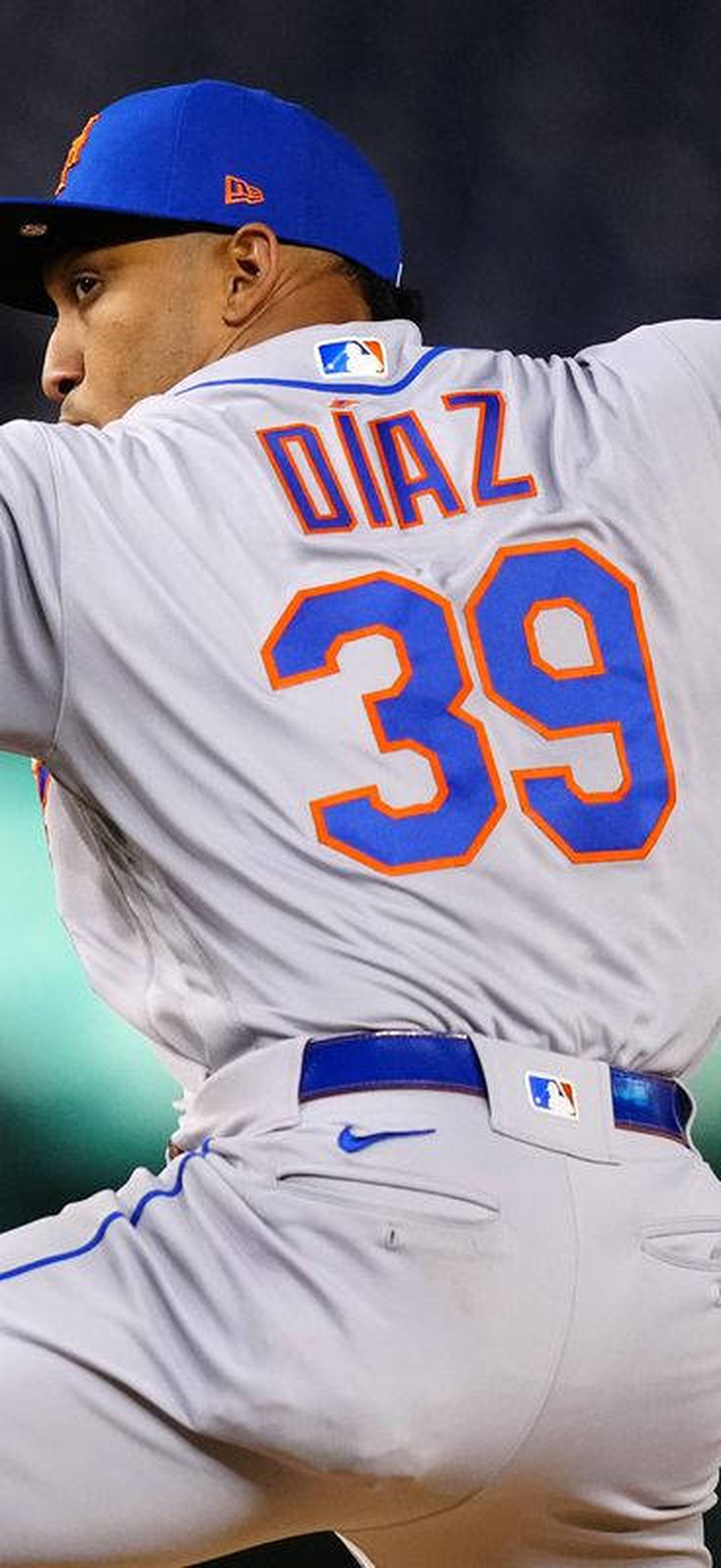 Baseball pitcher in Mets uniform mid-throw during night game.
