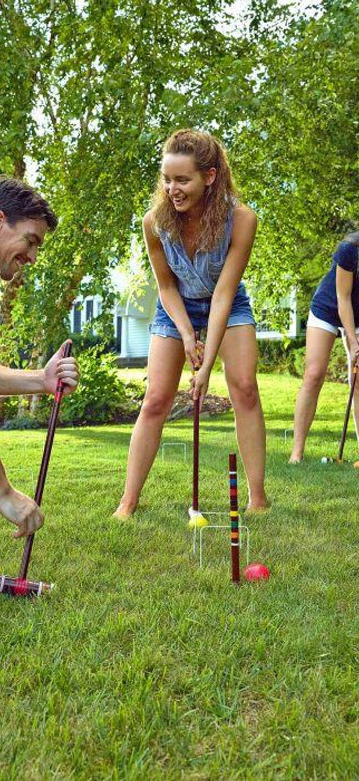 Four people playing croquet on a sunny lawn with trees in background.