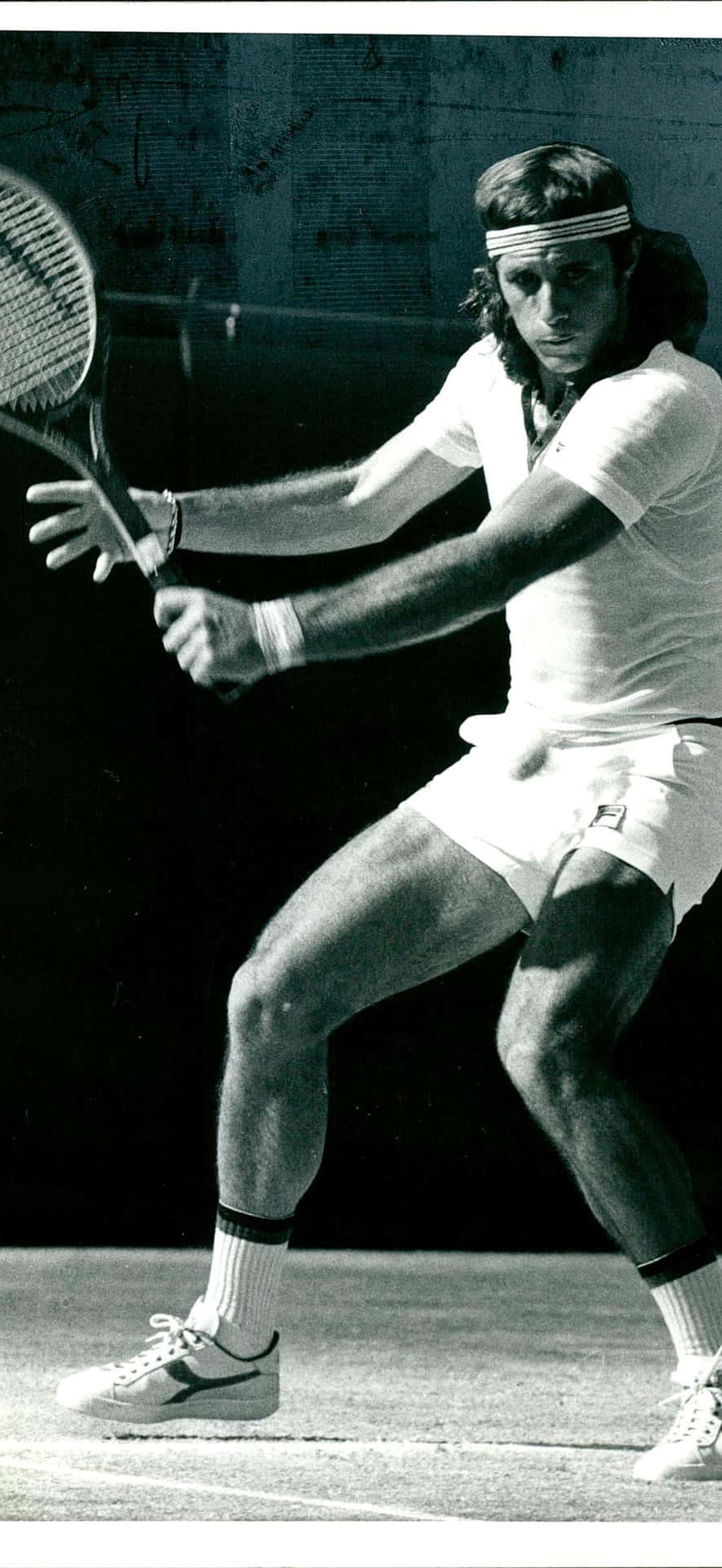 Male tennis player in vintage attire swinging racket on court.