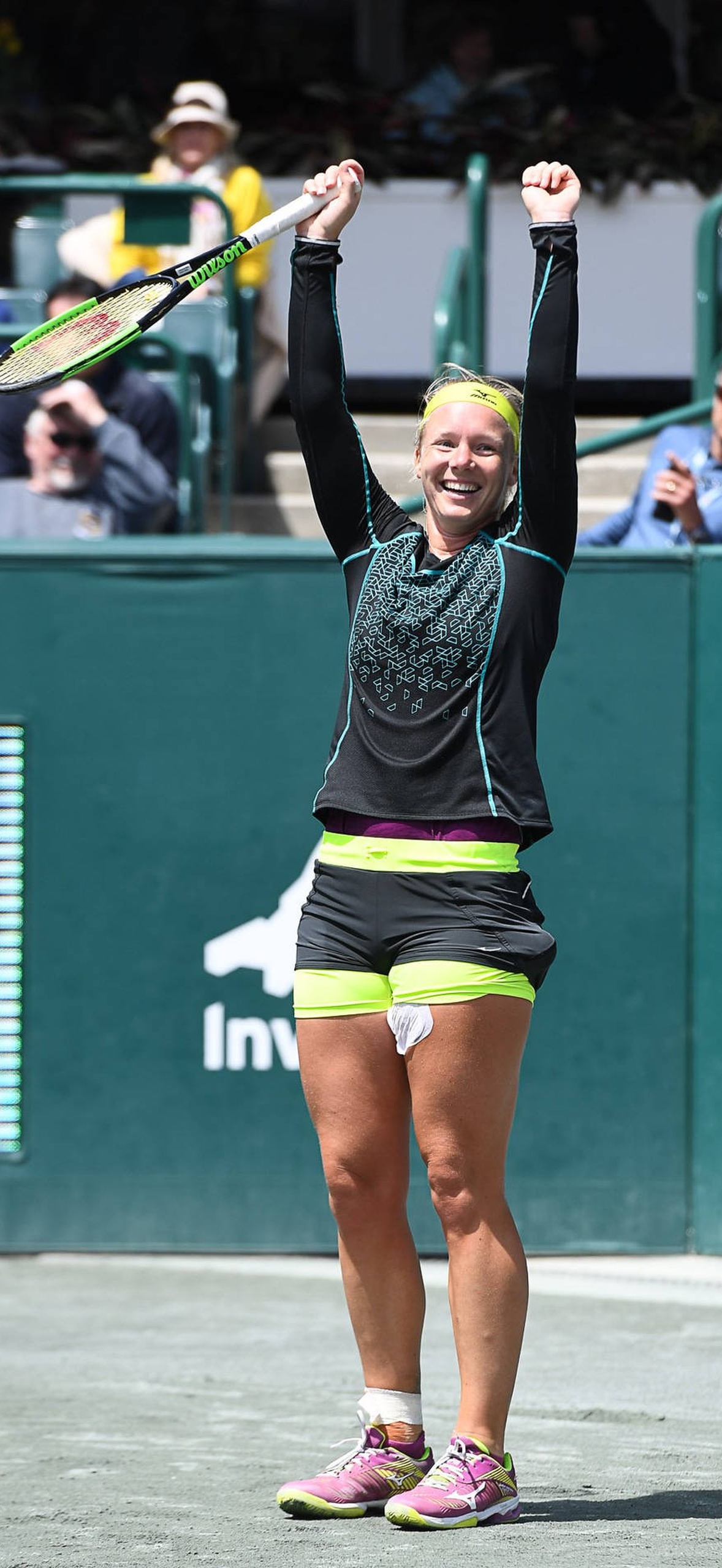 Tennis player triumphantly raises arms and racket after winning match.