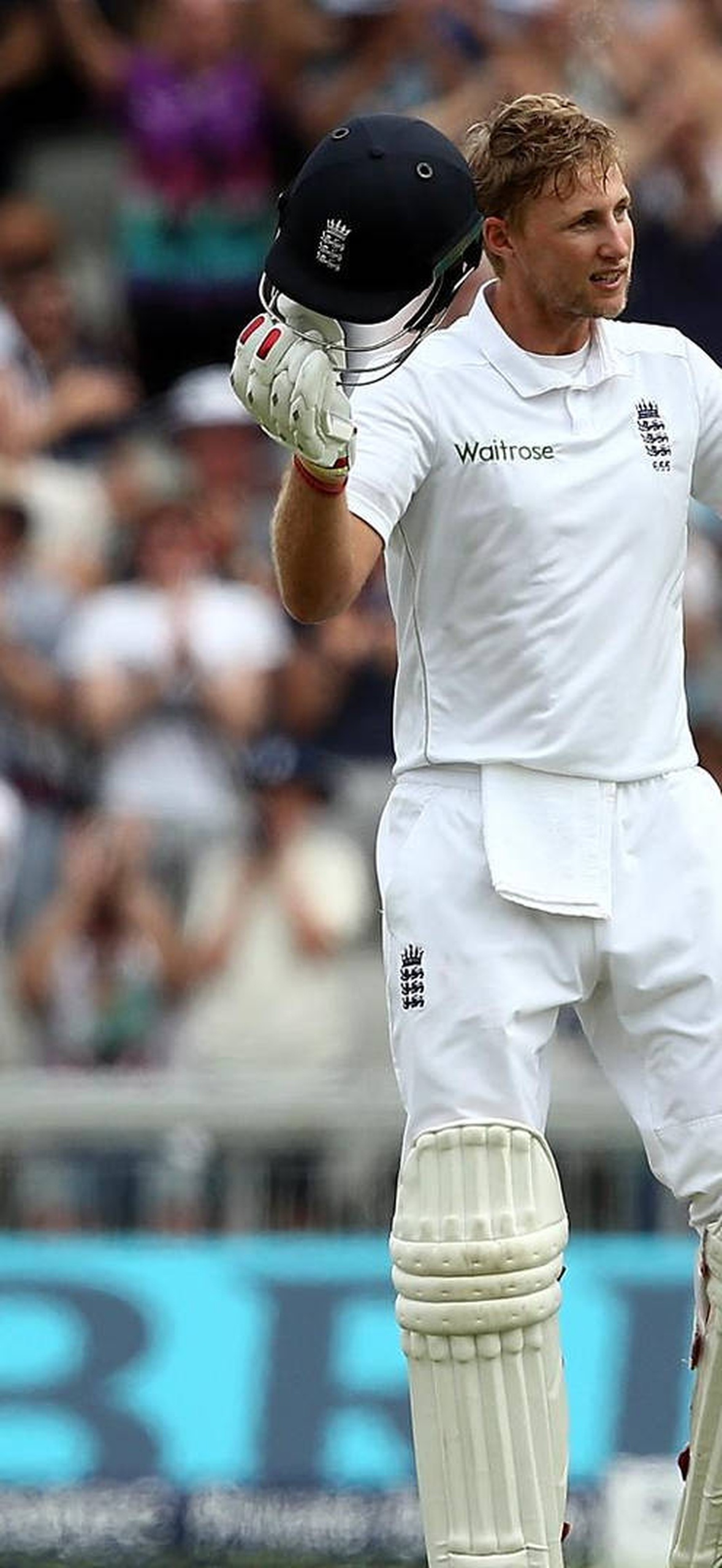 Cricket player celebrates with bat and helmet raised during daytime match.