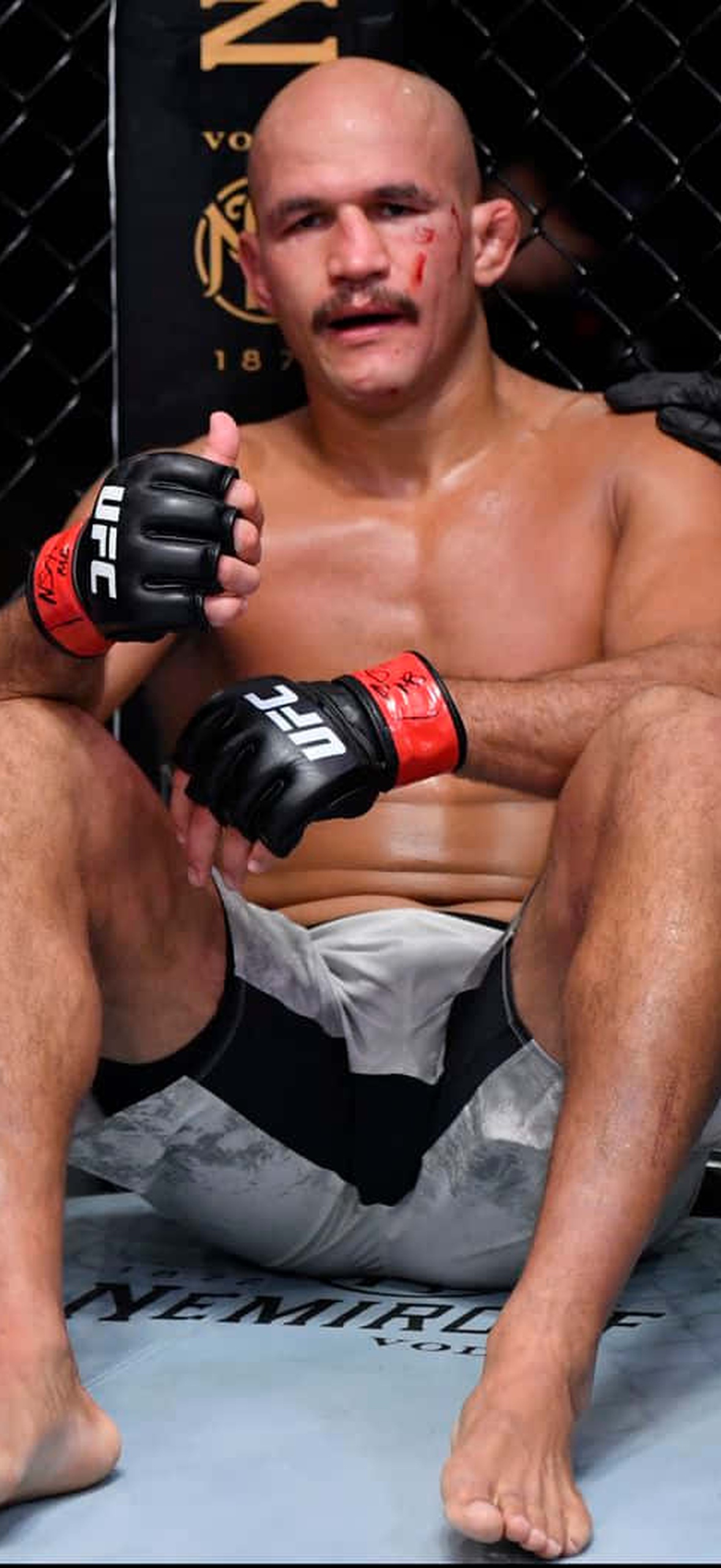 MMA fighter with bloody nose sitting on octagon floor after fight.