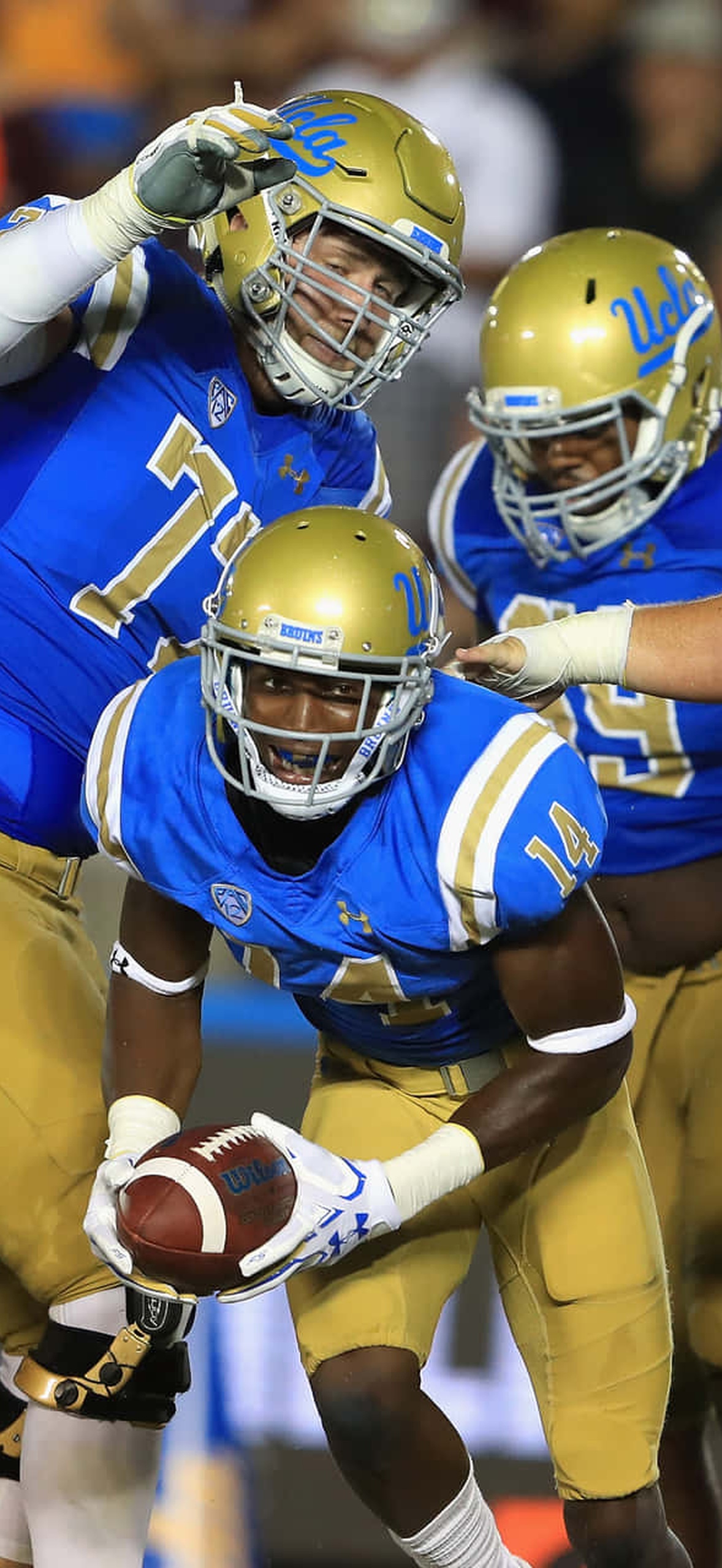 UCLA football players huddle around a teammate holding the ball after scoring.