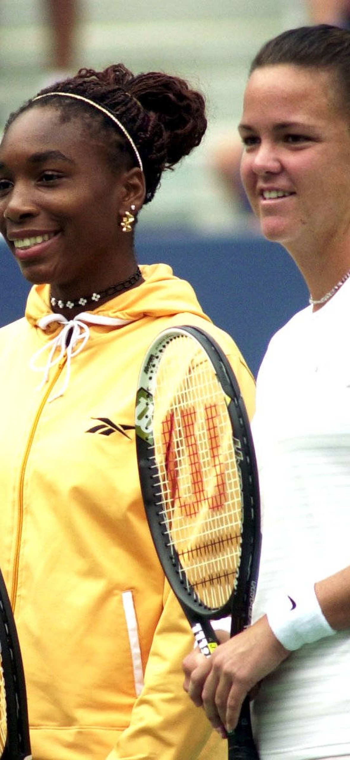 Two female tennis players smiling while holding rackets on a court.