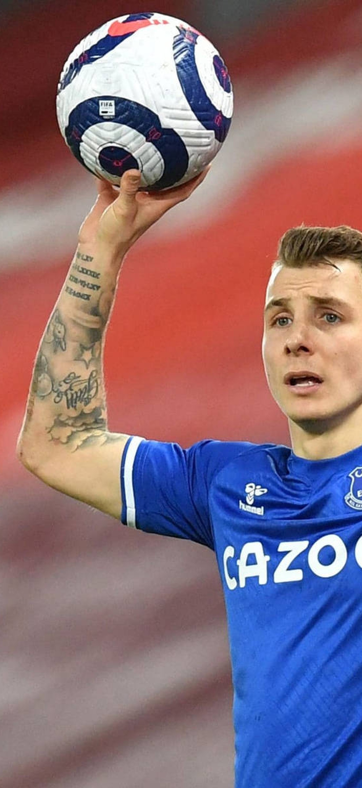 Footballer in blue jersey holding ball with tattoos visible in stadium