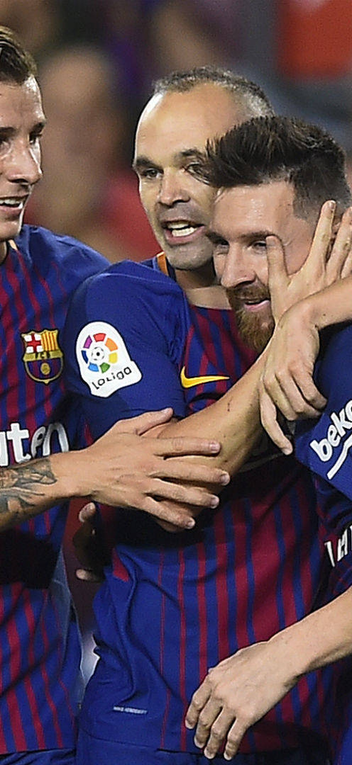 Three football players hugging after a goal in a stadium crowd.