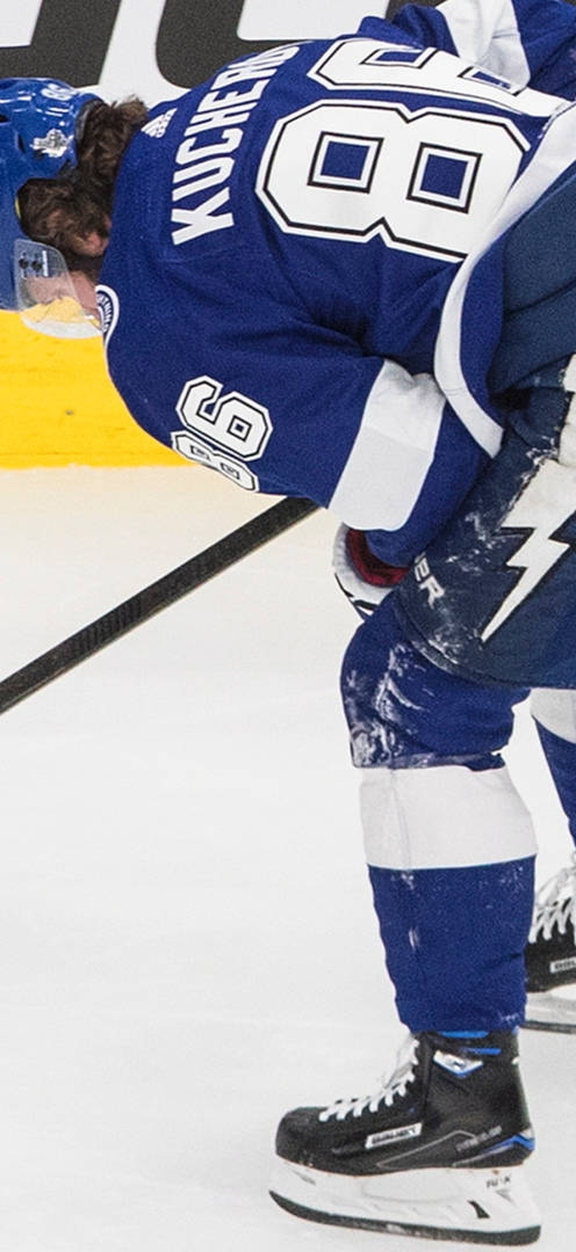 Hockey player in blue uniform bending over on ice rink.