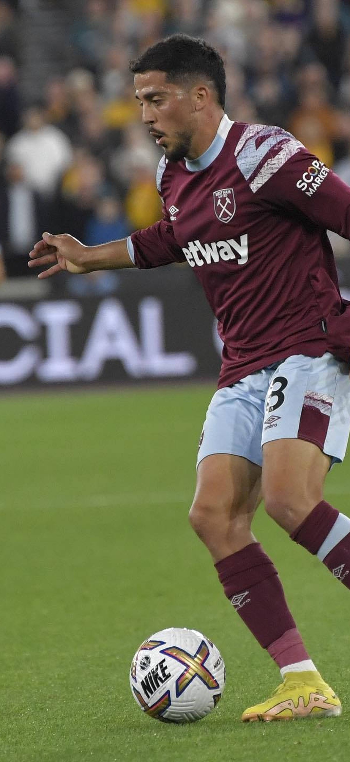 Football player dribbling a ball on a lit stadium field with spectators in background.