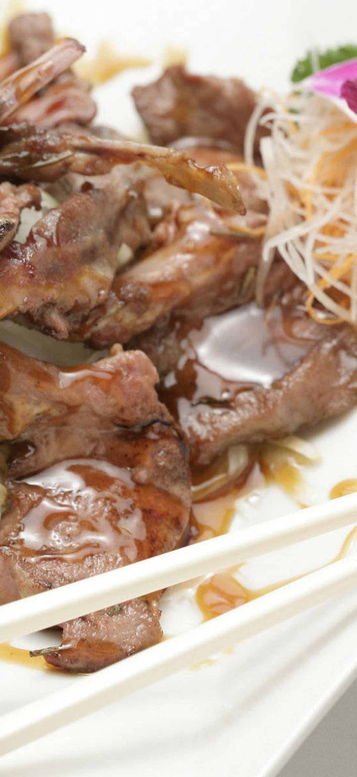 Sauced meat with rice and chopsticks garnished with pink orchid.