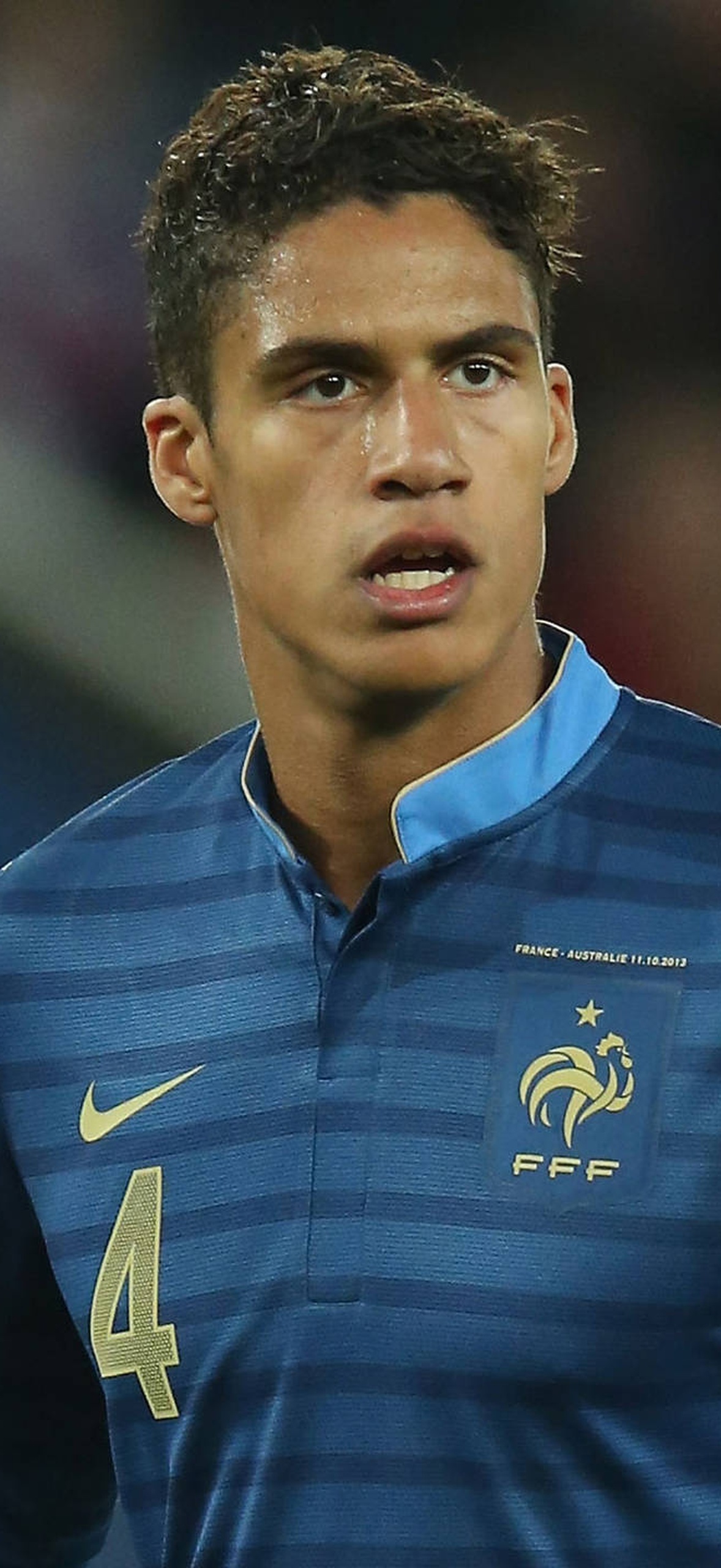 French football player wearing blue striped jersey with number 4 on field at night.