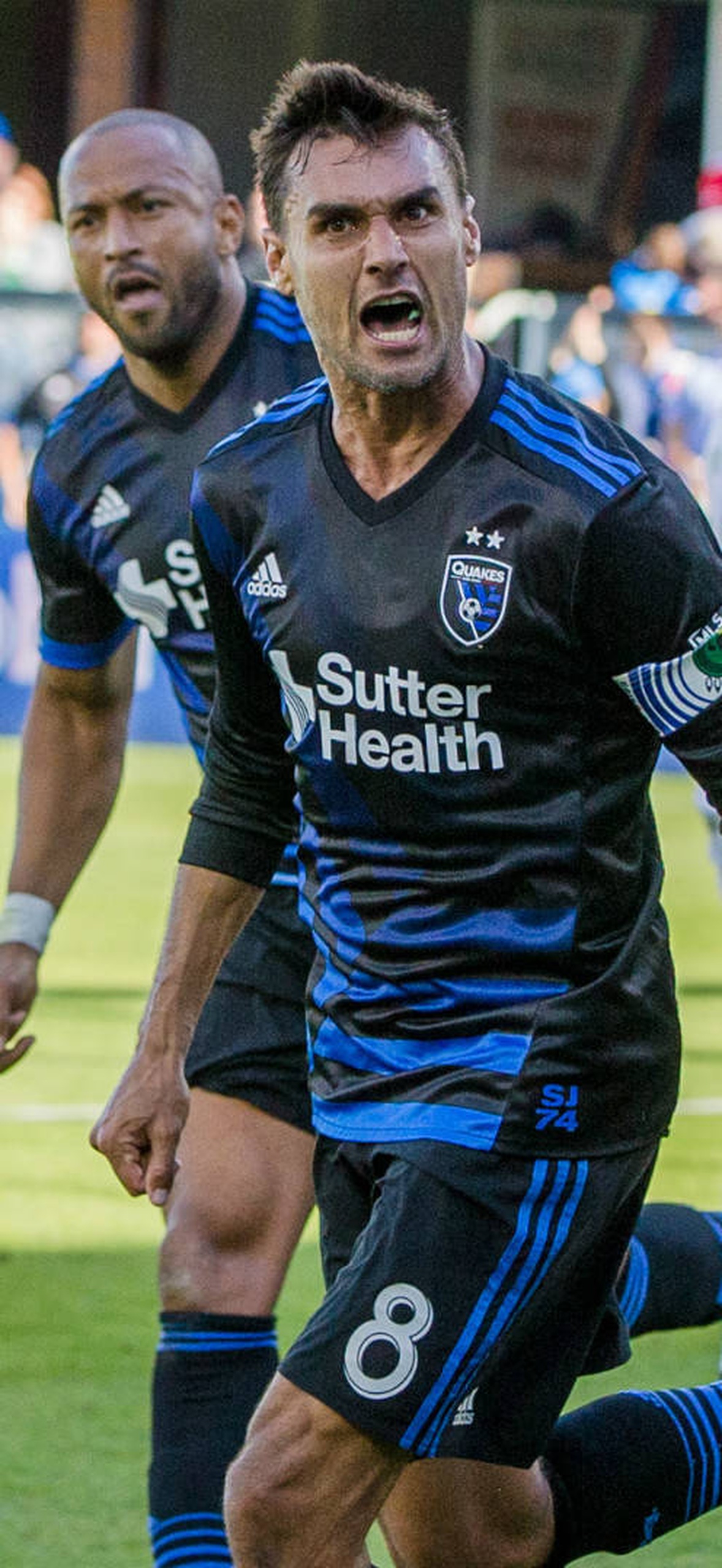 Soccer player celebrating a goal on a sunny field with fans watching.