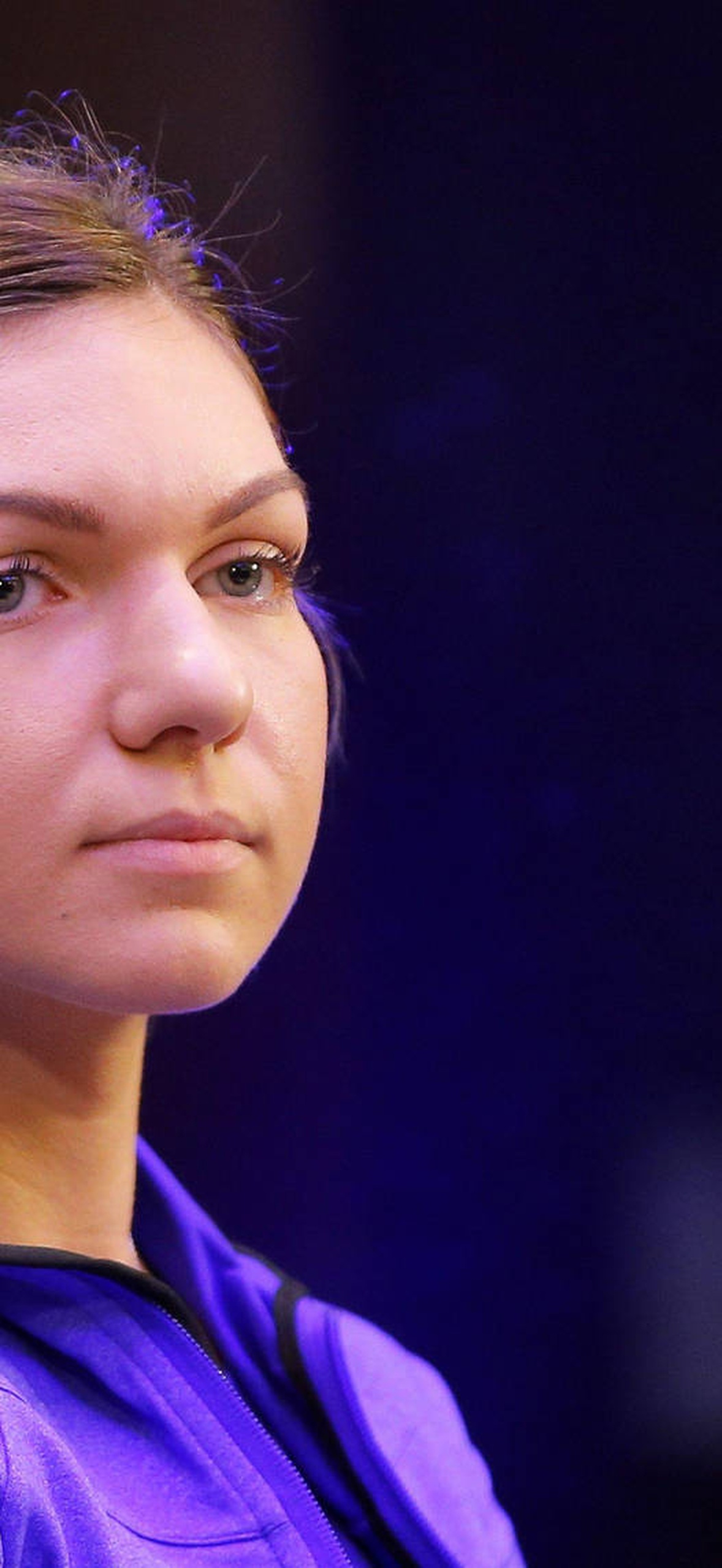 Serious young woman in purple athletic shirt looking off camera indoors.