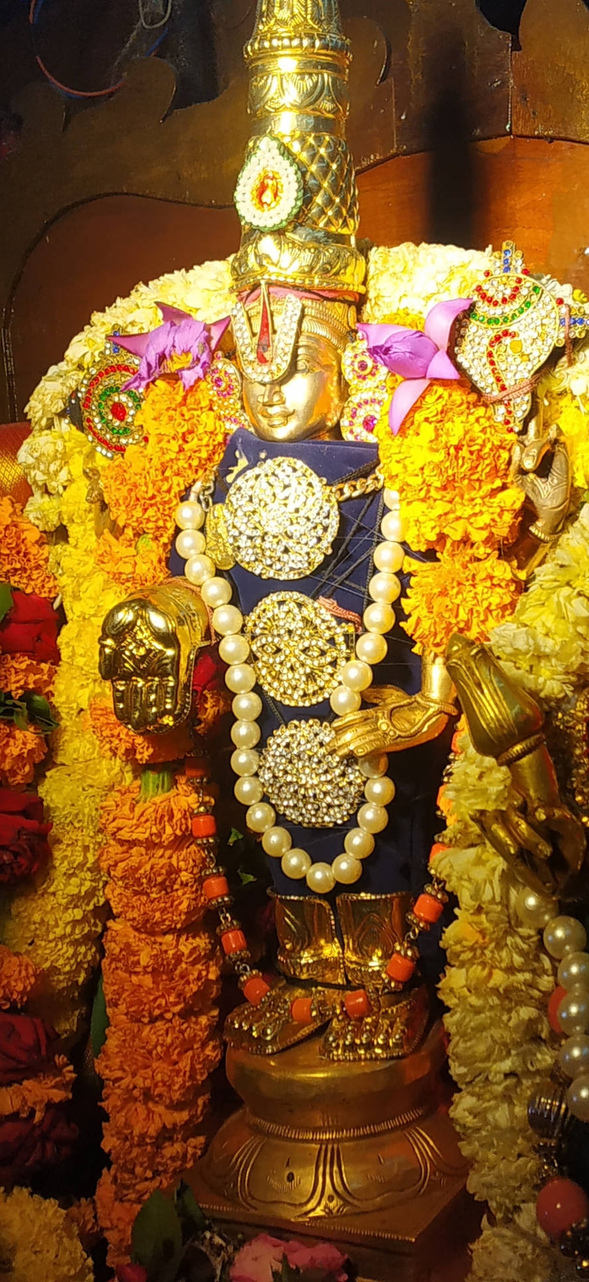 Golden deity statue decorated with marigold garlands and pearl jewelry in a temple.
