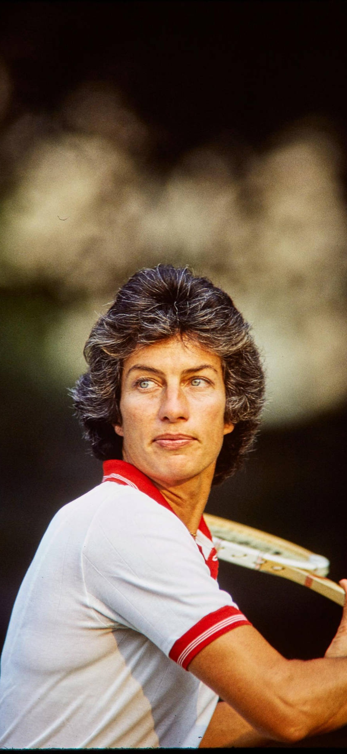 Male tennis player in white and red shirt holding racket mid-swing outdoors.