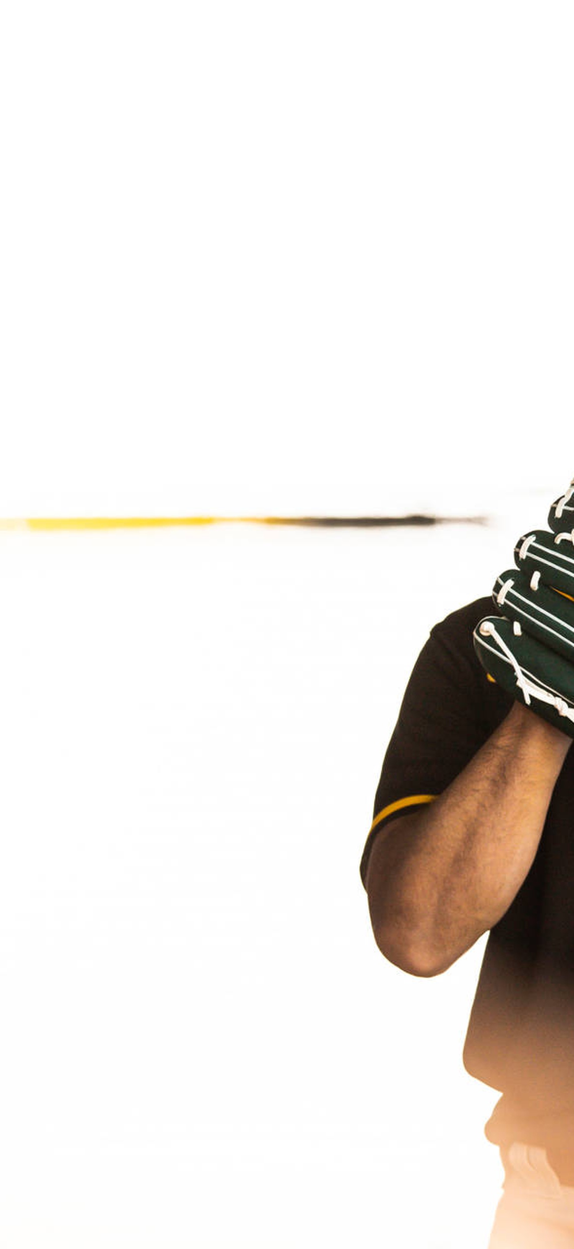 Baseball player in black and yellow uniform holding glove at sunset.