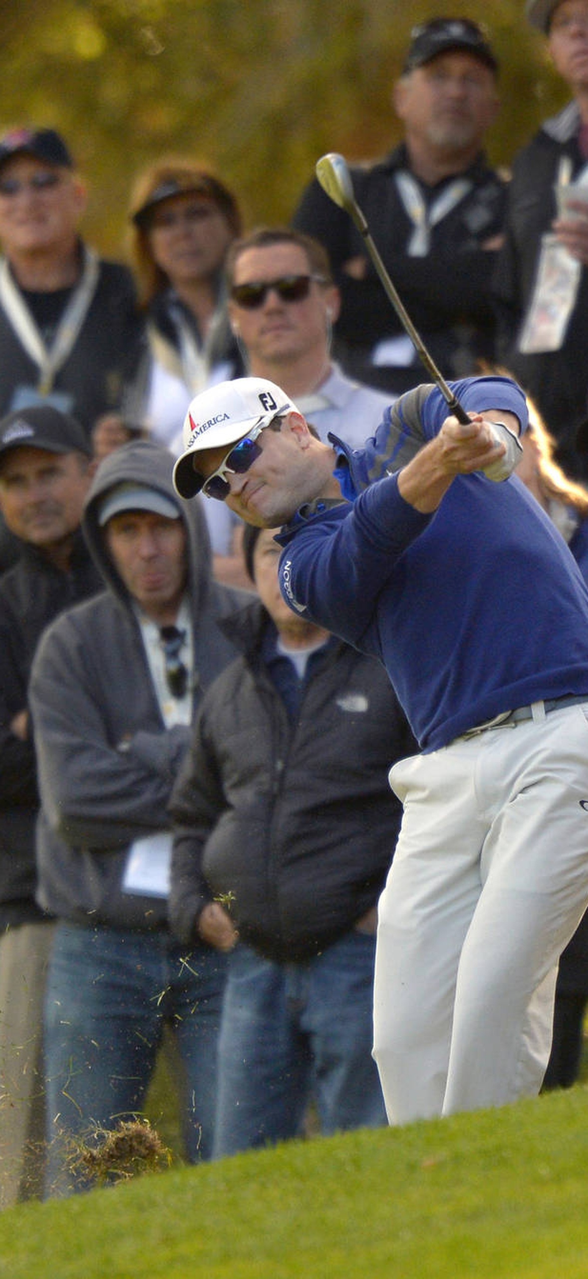 Golfer hitting sand shot with crowd watching in autumn.